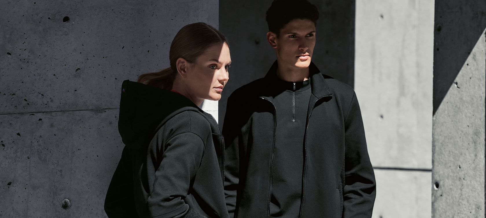 Un couple est dans l'ombre. Une femme présente la veste sweat BMW pour femme et un homme porte la veste sweat BMW pour homme.